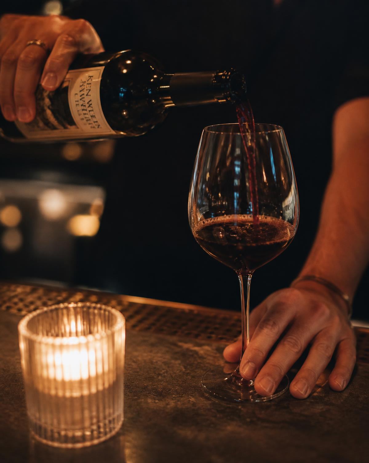 A glass of red wine being poured at the bar counter